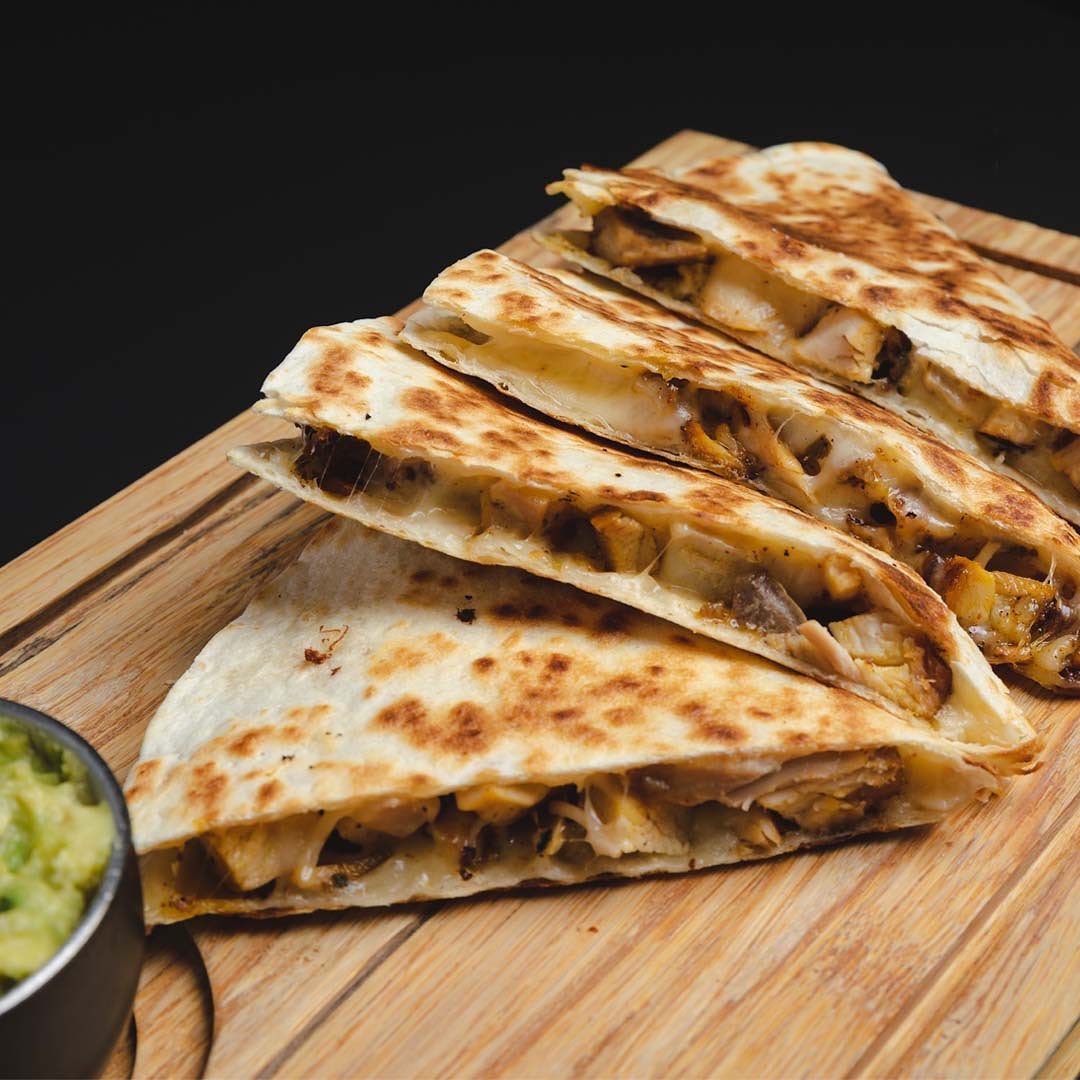 Chicken quesadilla slices with guacamole on a wooden board
