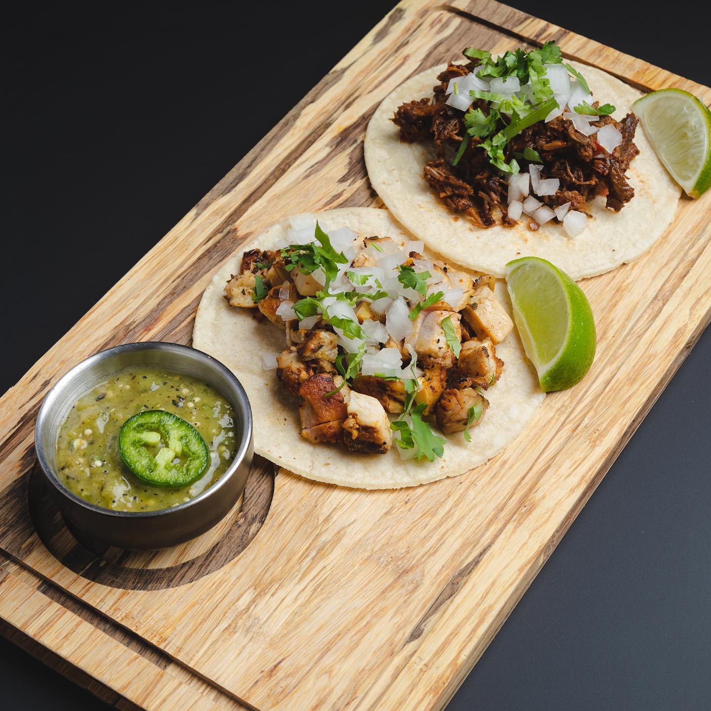 Carnitas and chicken tacos with salsa verde on a wooden board